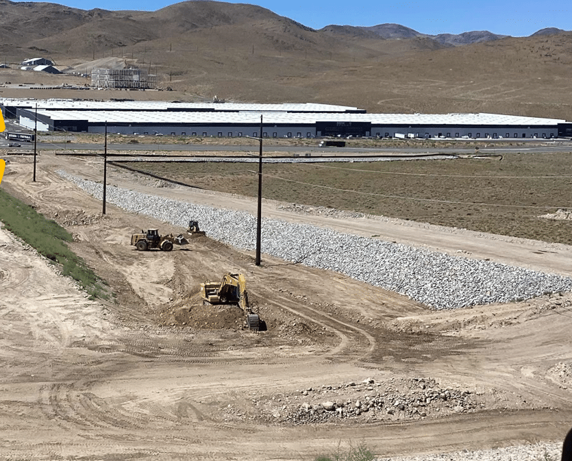 Bulldozers working on site prep near gravel-lined channel and industrial buildings.
