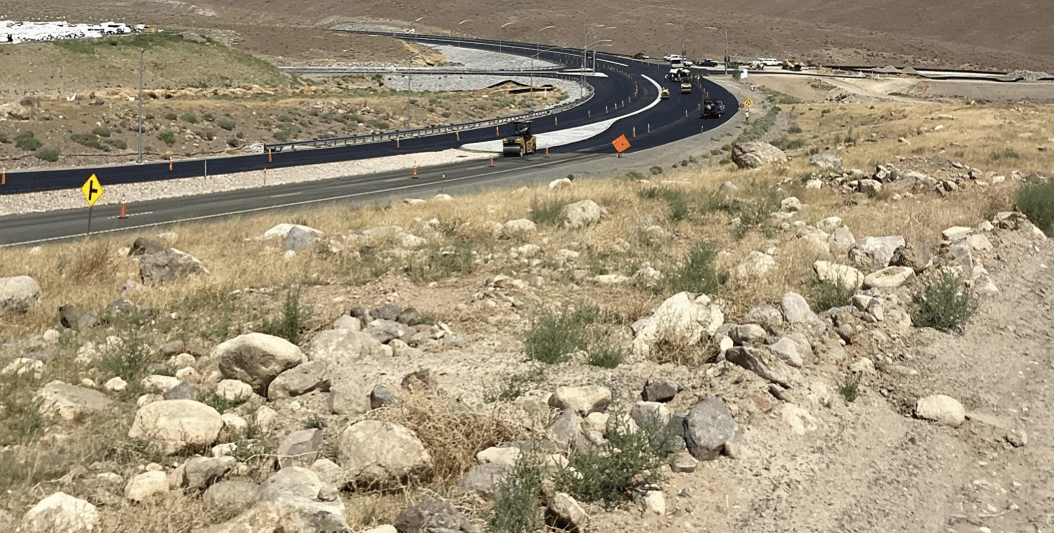 Paved road winding through dry, rocky terrain with construction signs and equipment.