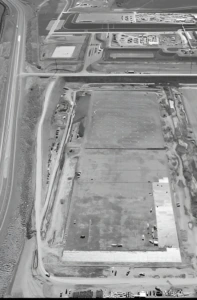 Top-down image of construction site beside highway and industrial buildings.